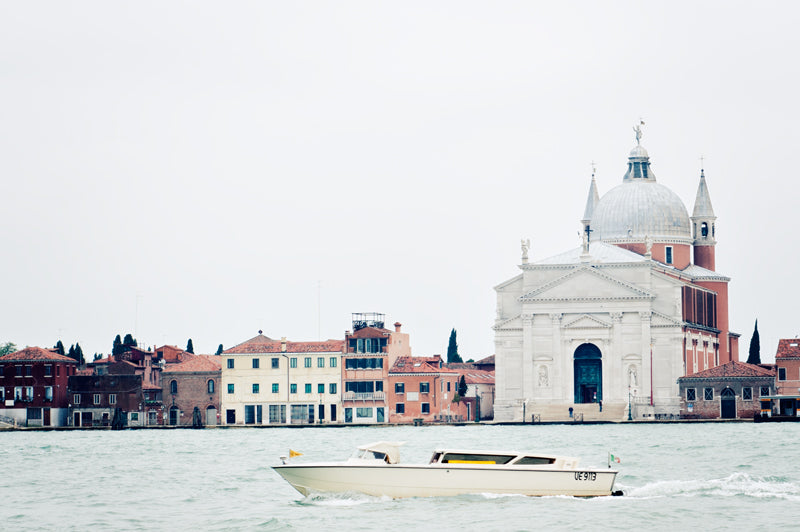 A boat cruises on a canal in Venice, the beautiful architecture of this city features  in the background