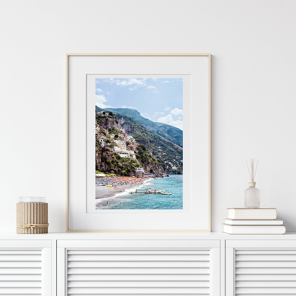 Amalfi coast fine art print featuring the Spaggia Grande Beach in Positano, the village, houses, the cliffs, the orange beach umbrellas and the jetty and blue mediterranean sea by Millie Brown