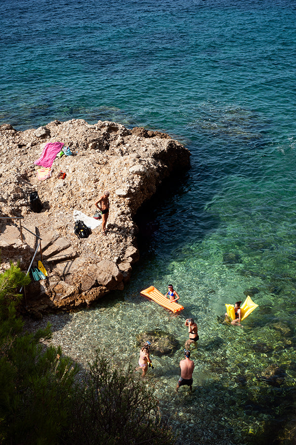 French Riviera beach print shot from above with swimmers in the sea and a rocky outcrop with beach towels and a swimmer 