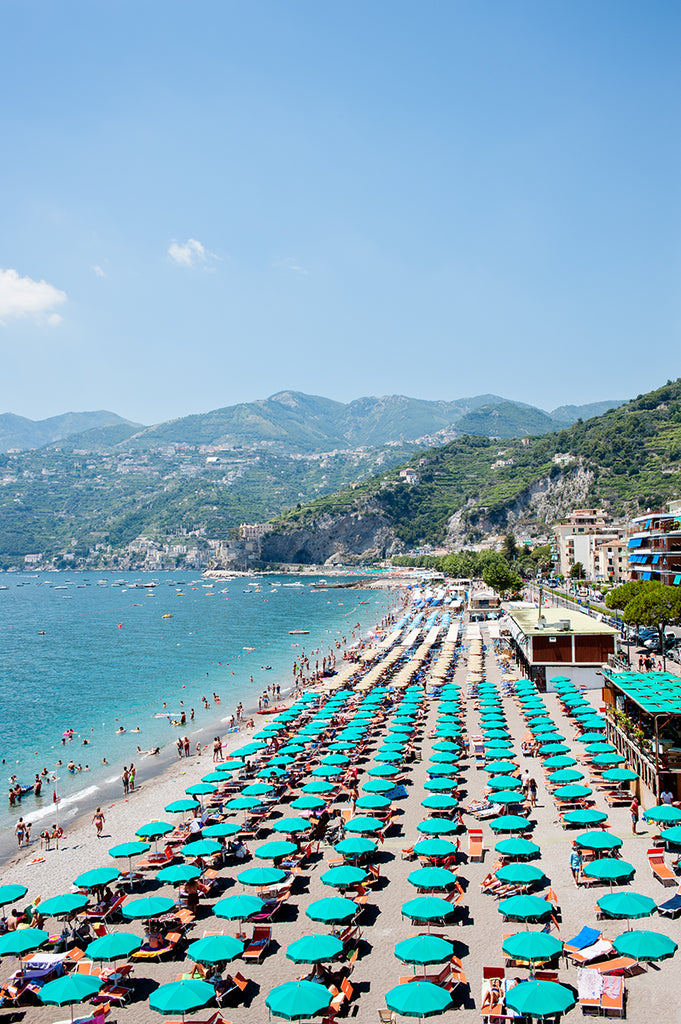 Amalfi Coast photographic print featuring Amalfi beach with its emerald green umbrellas lined up 8 deep and the blue mediterranean se and green rolling hills beyond.