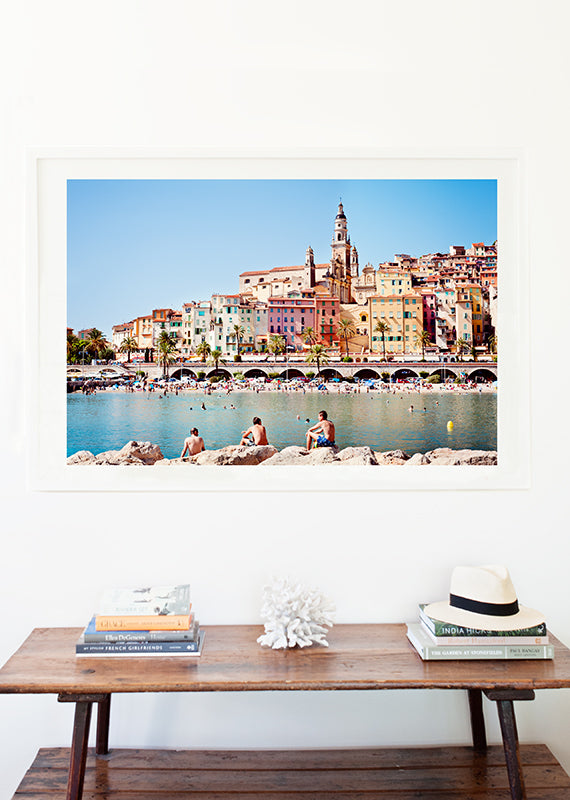 French Riviera limited edition print featuring the beautiful colourful village of Menton and it's beach with the blue mediterranean in the foreground and swimmers on the rocks by professional photographer Millie Brown