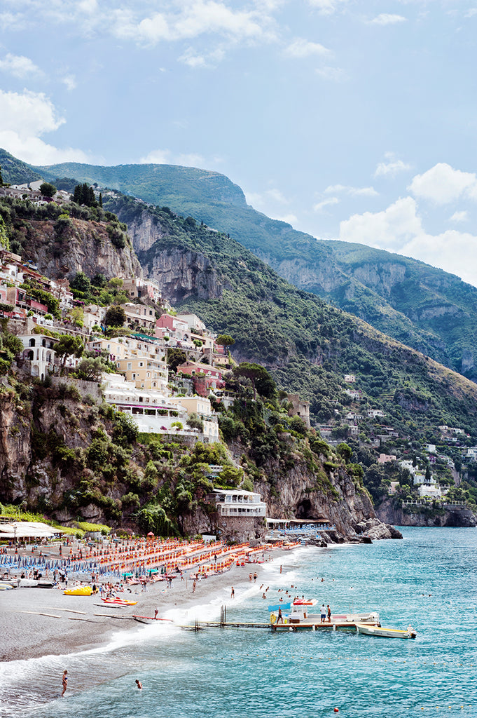 Amalfi coast print featuring the Positano beach with the village, houses, the cliffs, the orange beach umbrellas and the jetty and blue mediterranean sea by Millie Brown