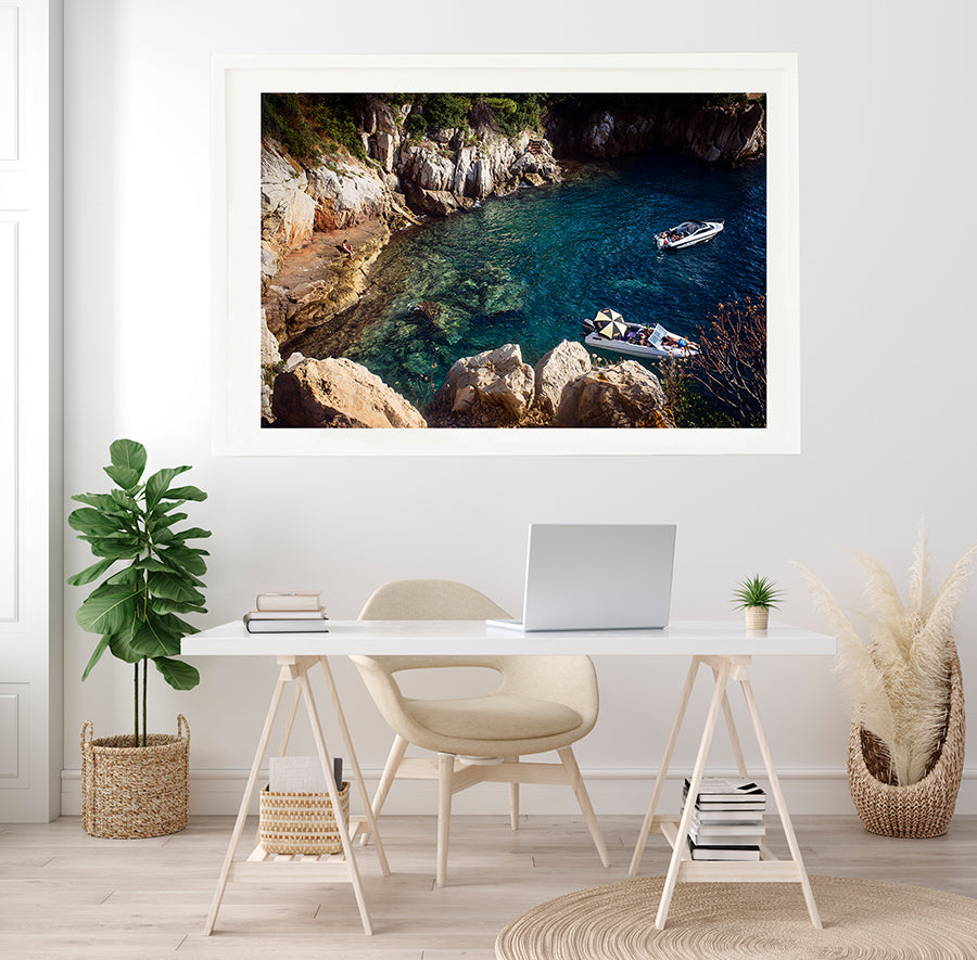French Riviera Fine Art Wall print of summer in a Cap Ferrat swimming cove,  the blue mediterranean sea in a small cove on Cap Ferrat with a person sitting on the rocks and two leisure boats with people sun bathing by travel photographer Millie Brown
