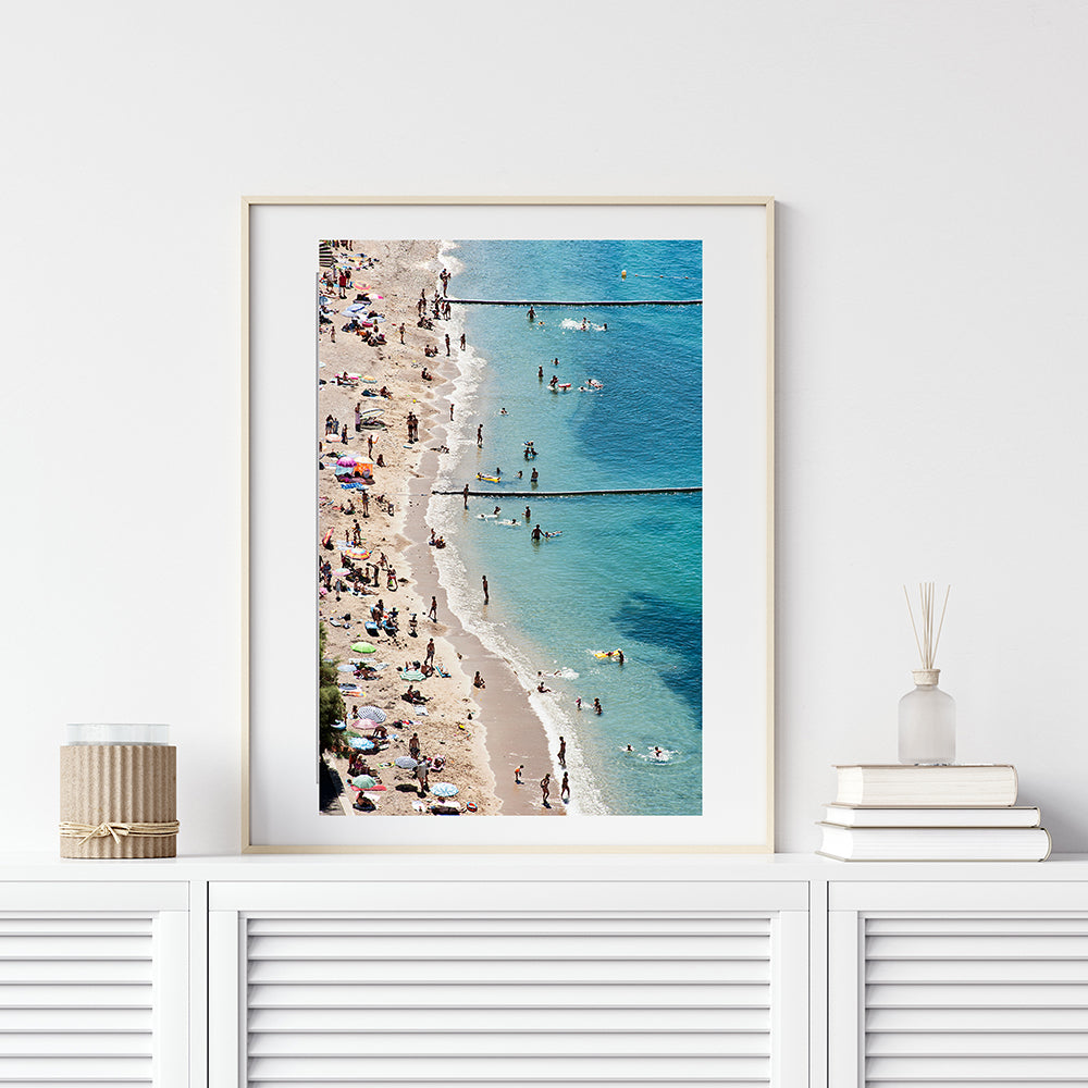 French Riviera print featuring the beautiful and busy Villefranche sur Mer beach on a hot summer day. People swimming and lying on the beach with colourful beach umbrellas dotting the beach