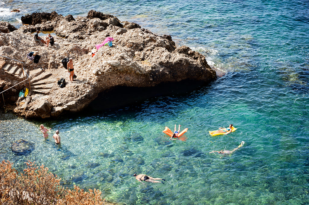 Cote d'azur wall art prints featuring the French Riviera and a small beautiful swimming cove surrounded by rocks and showing people swimming in the blue mediterranean sea, shot from above by travel photographer Millie Brown