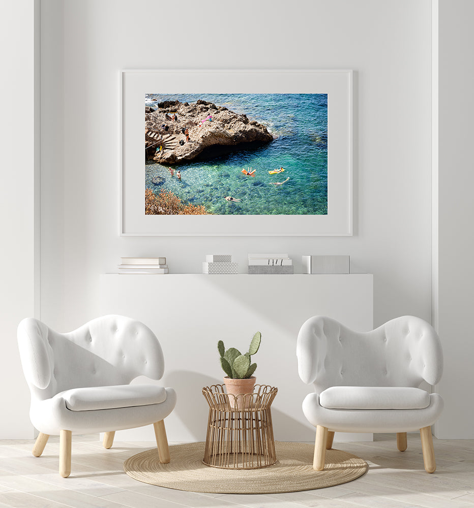 French Riviera Cote d'azur wall art prints featuring the French Riviera and a small beautiful swimming cove surrounded by rocks and showing people swimming in the blue mediterranean sea, shot from above by travel photographer Millie Brown